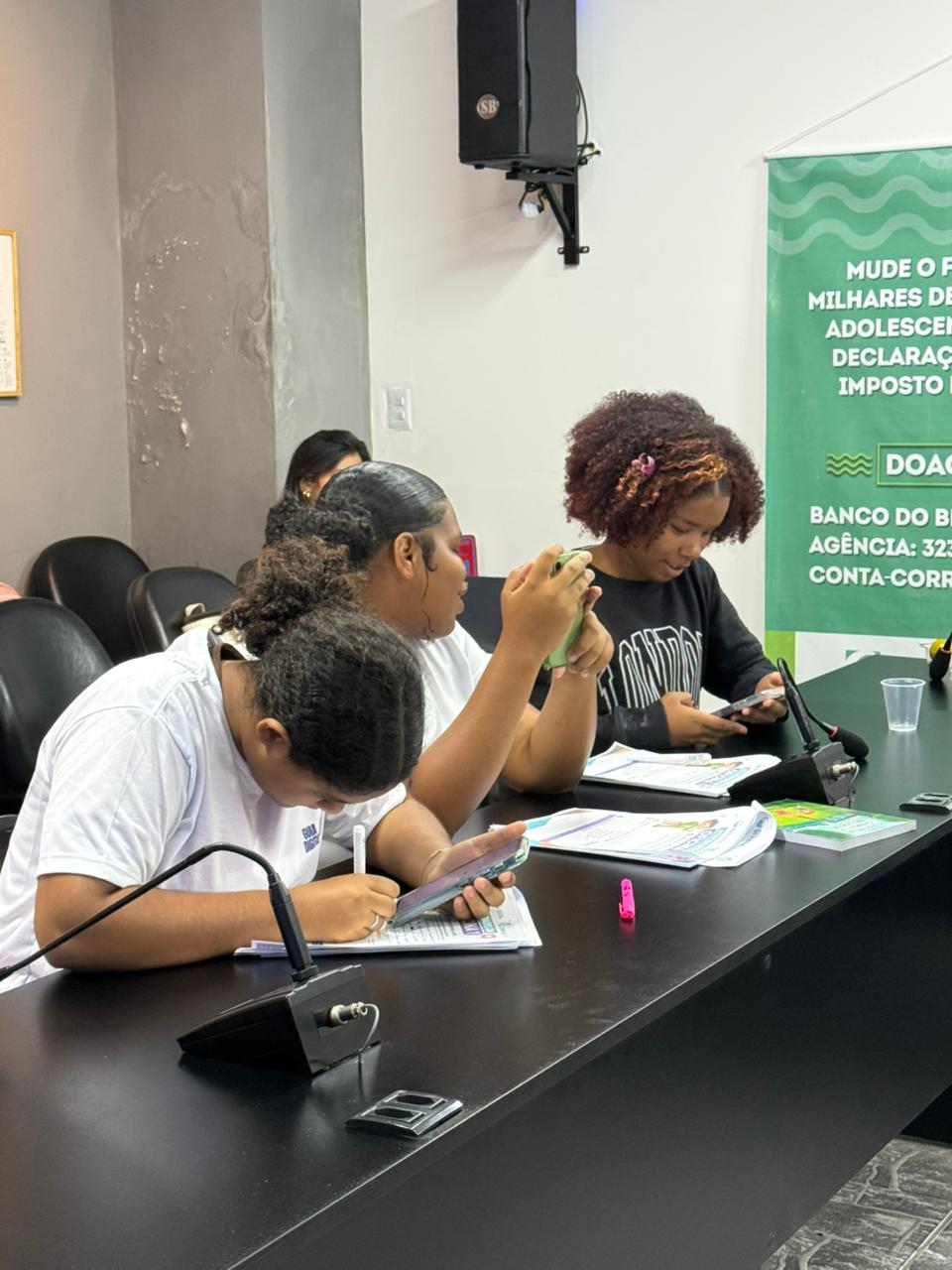 Jovens à mesa utilizam celulares e materiais impressos em uma atividade do Guia Digital Teen.